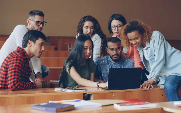 Students working together around a laptop in a classroom
